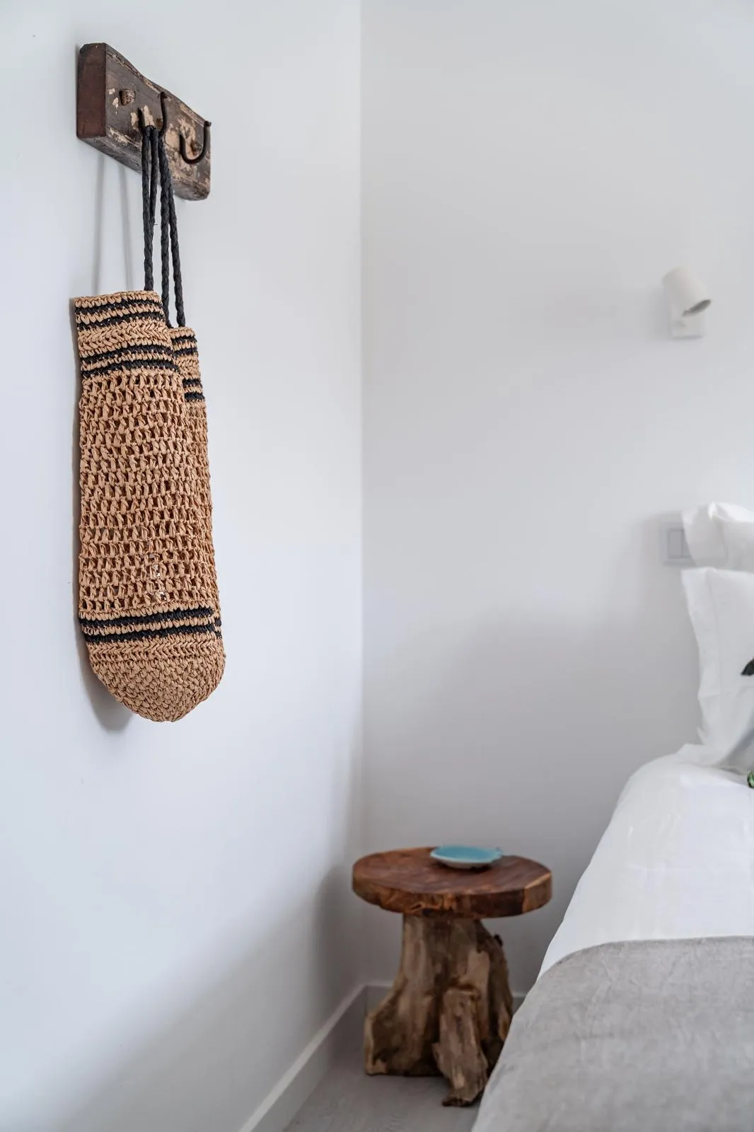 Bedroom detail with woven straw tote bag on rustic hook rack and tree-stump side table