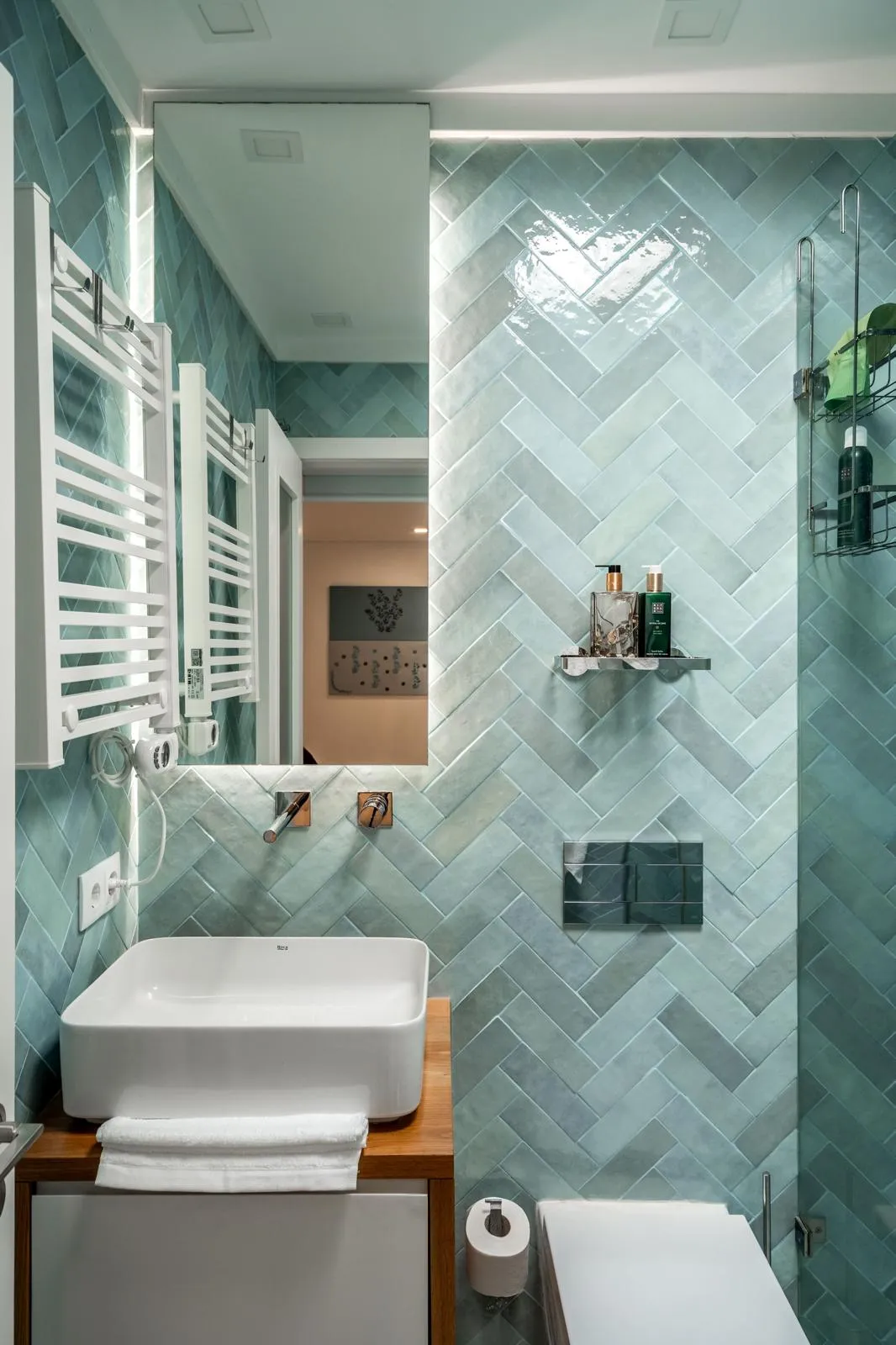 Bathroom with blue herringbone tiles, vessel sink on wood vanity, wall-mounted toilet and mirror cabinet