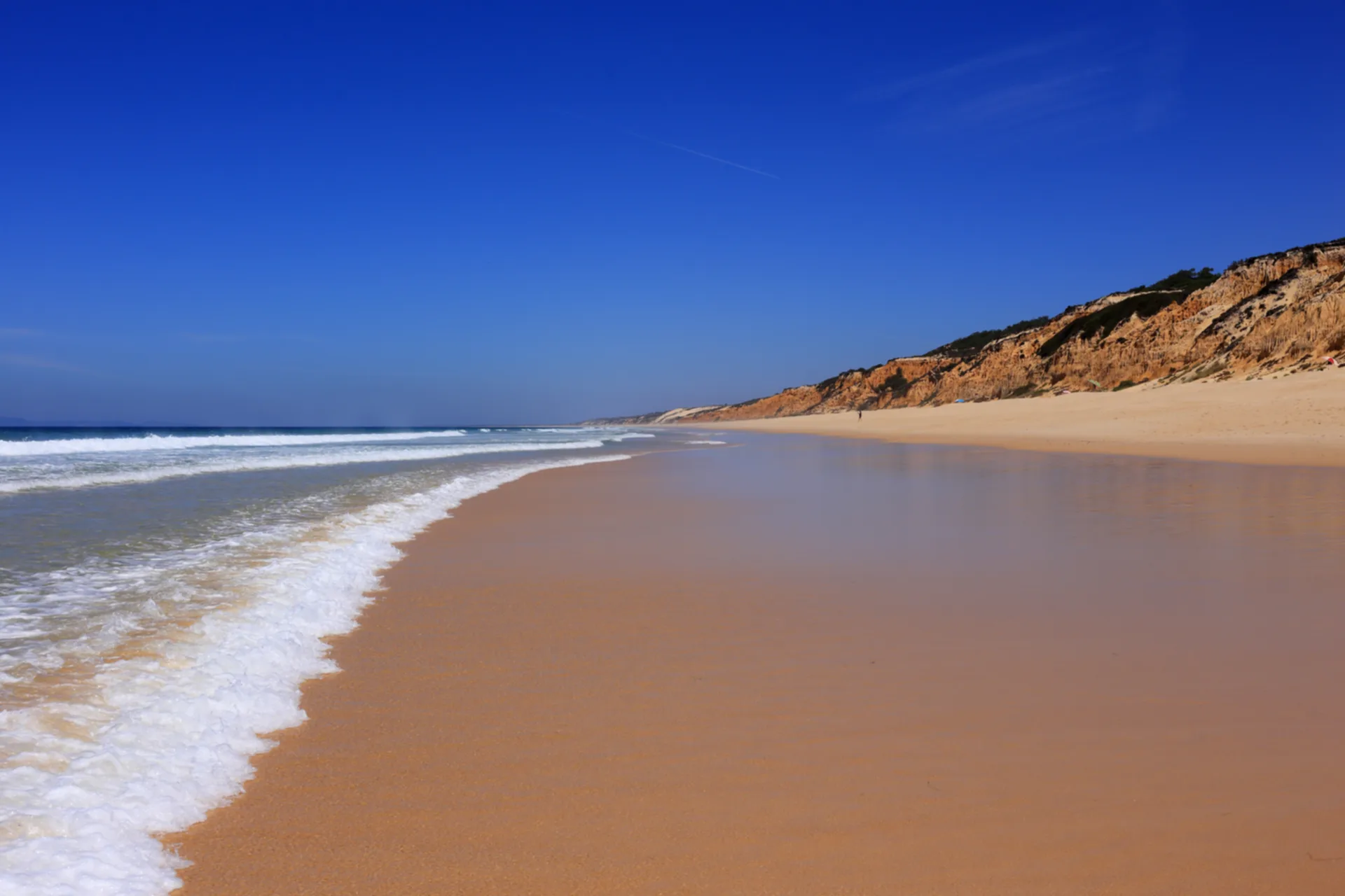 Long sandy beach with golden cliffs and rolling Atlantic waves
