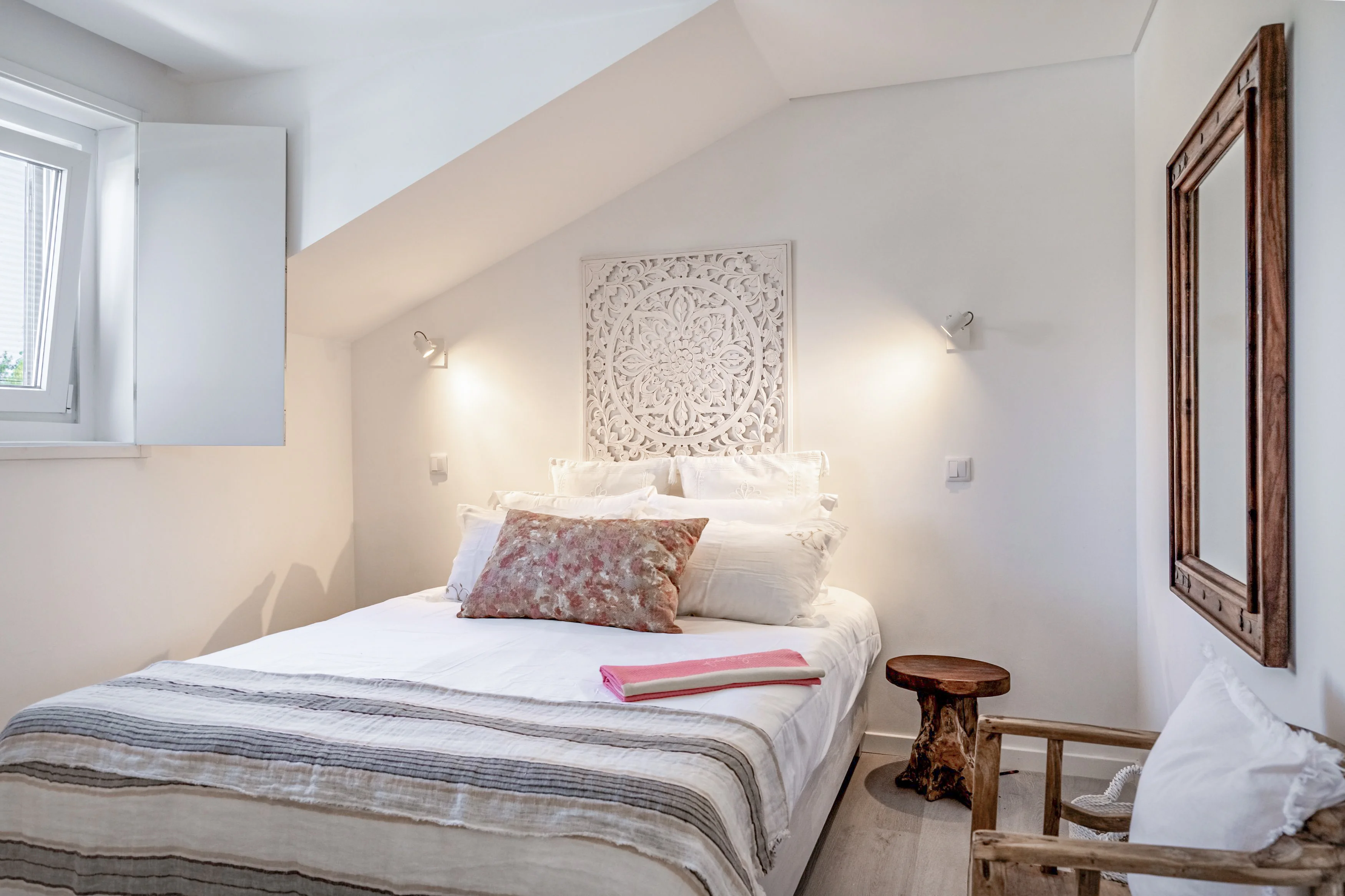 Attic bedroom with carved mandala headboard, reading sconces and ornate distressed mirror