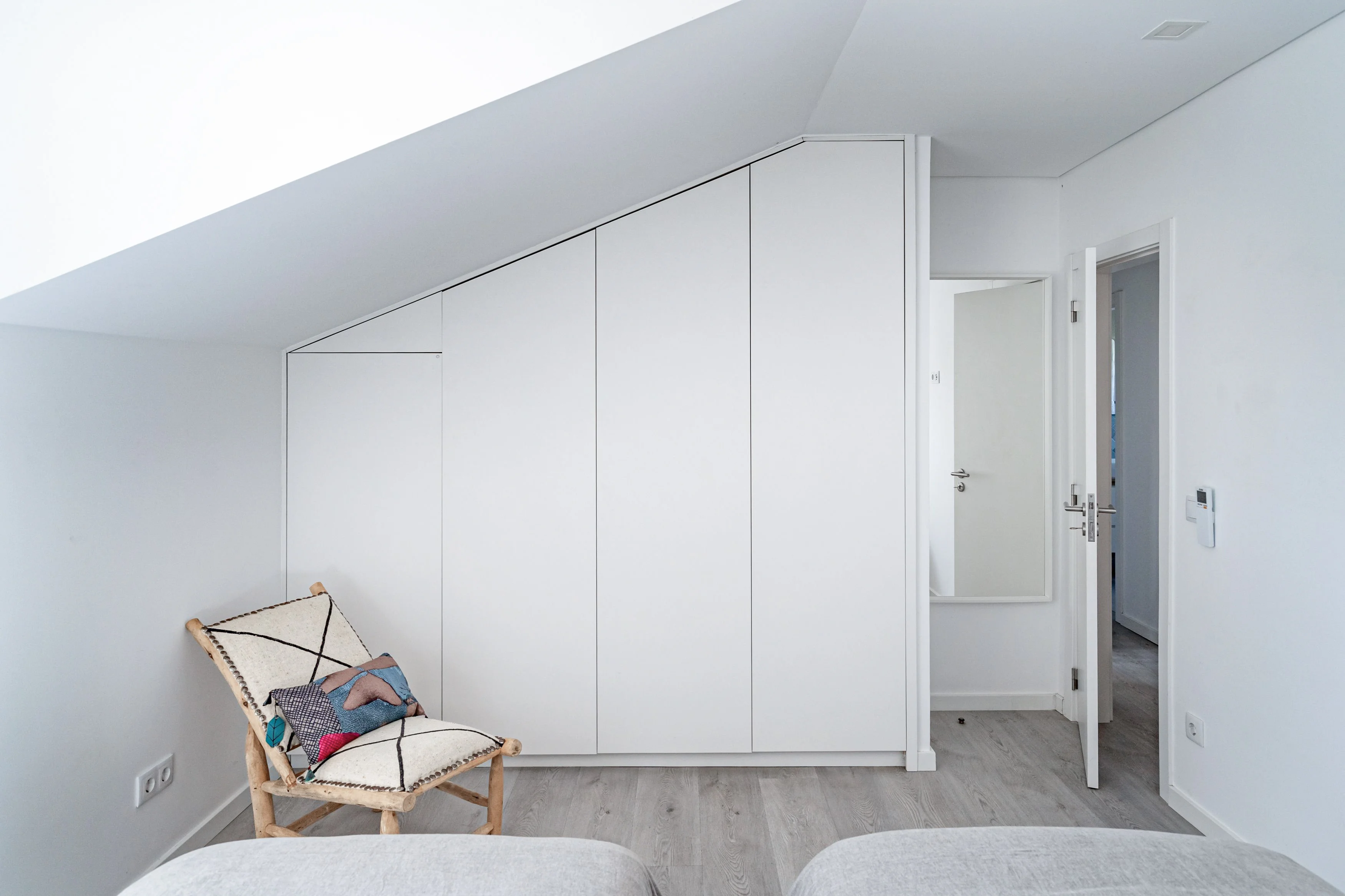 Attic bedroom with built-in wardrobe and bohemian sling chair under sloped ceiling