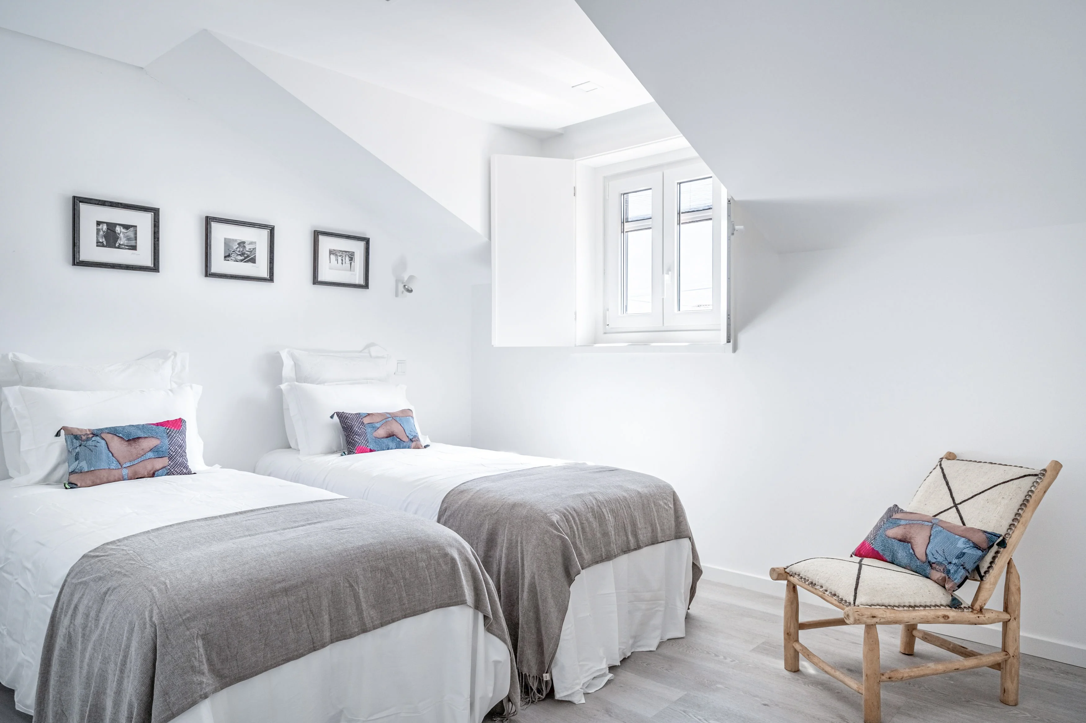 Twin bedroom with sloped ceiling, two single beds with white bedding and wooden armchair
