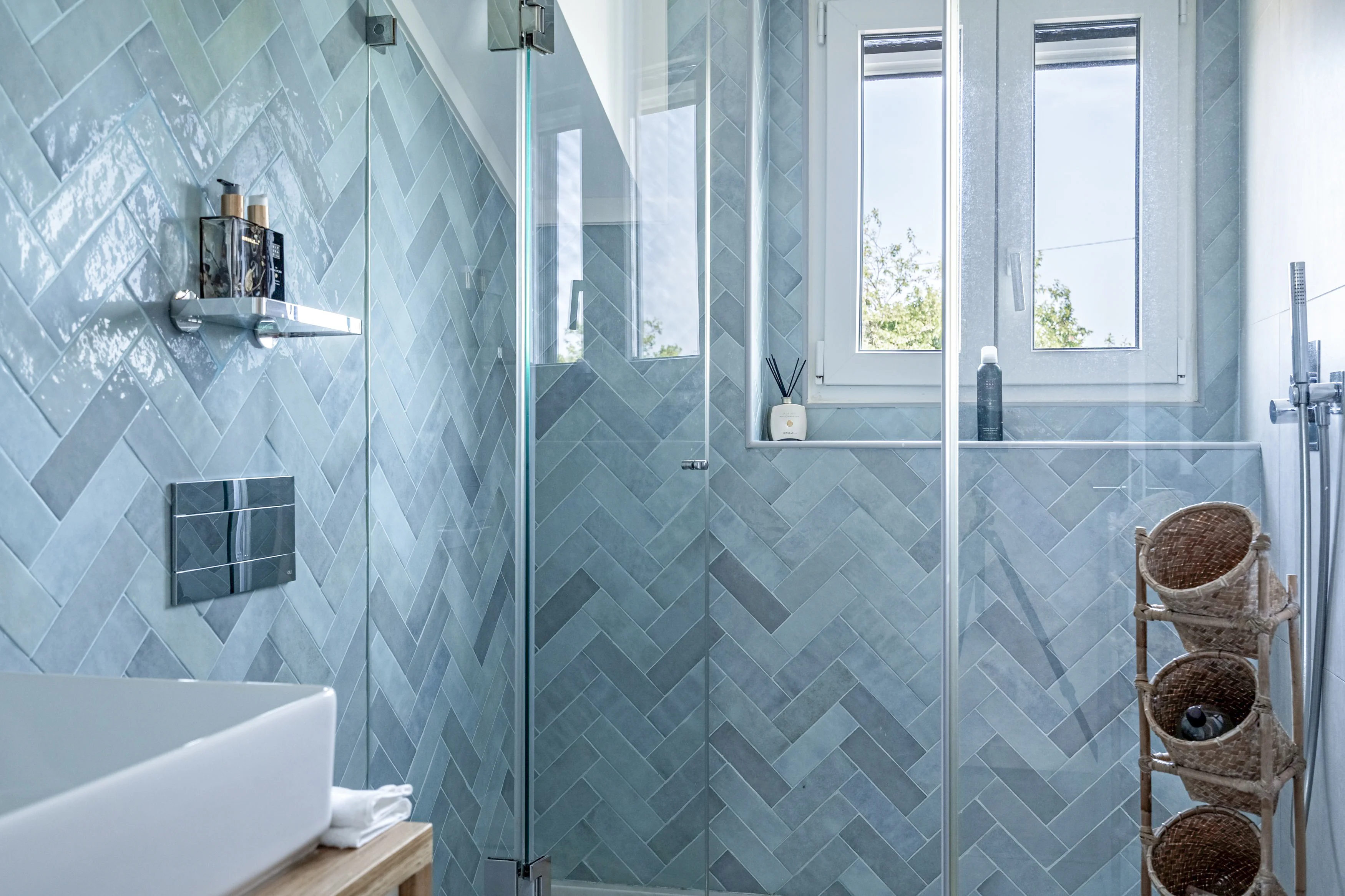 Bathroom with blue herringbone zellige tiles, glass shower, rainfall showerhead and window overlooking the garden