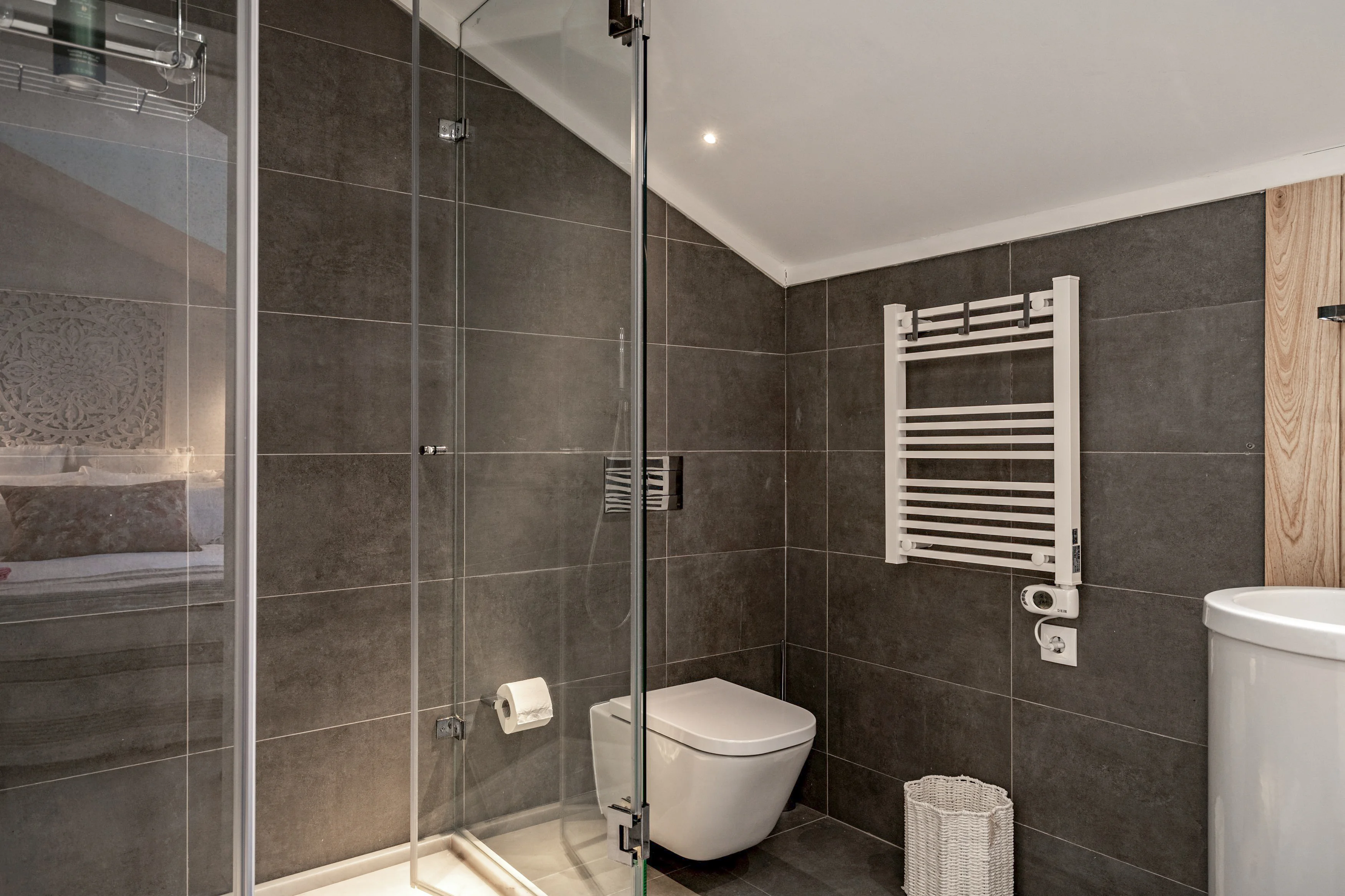 Bathroom with frameless glass shower, heated towel rail and dark tiles