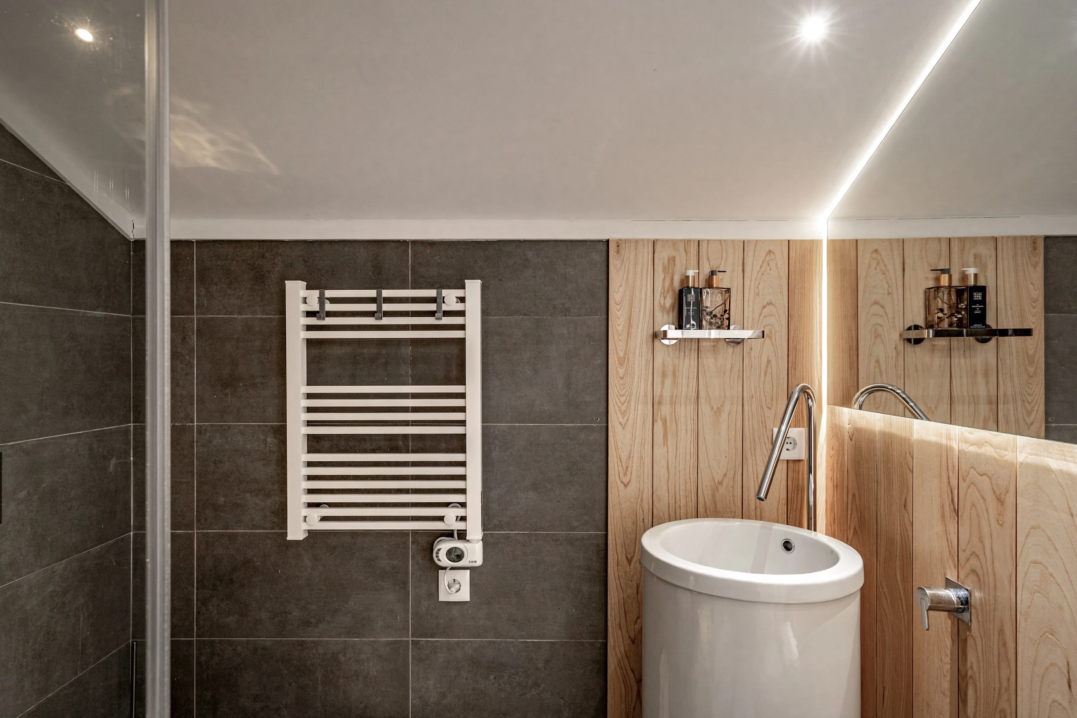 Modern bathroom with dark charcoal tiles, wood paneling, vessel sink and Rituals toiletries