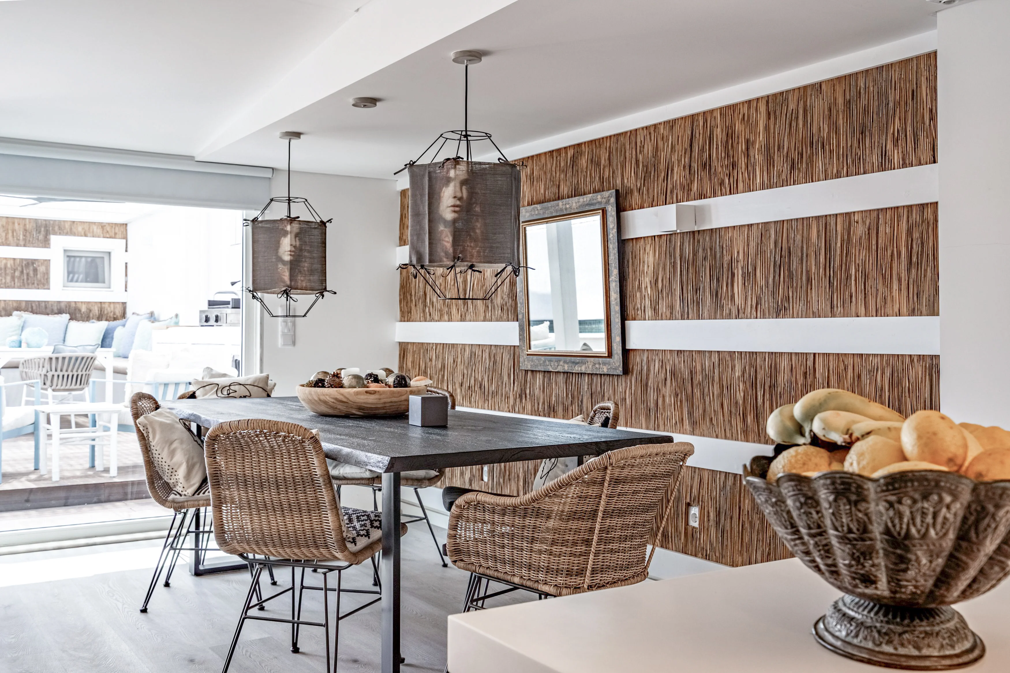 Dining room with rustic table, rattan chairs and portrait pendant lights over bamboo accent wall