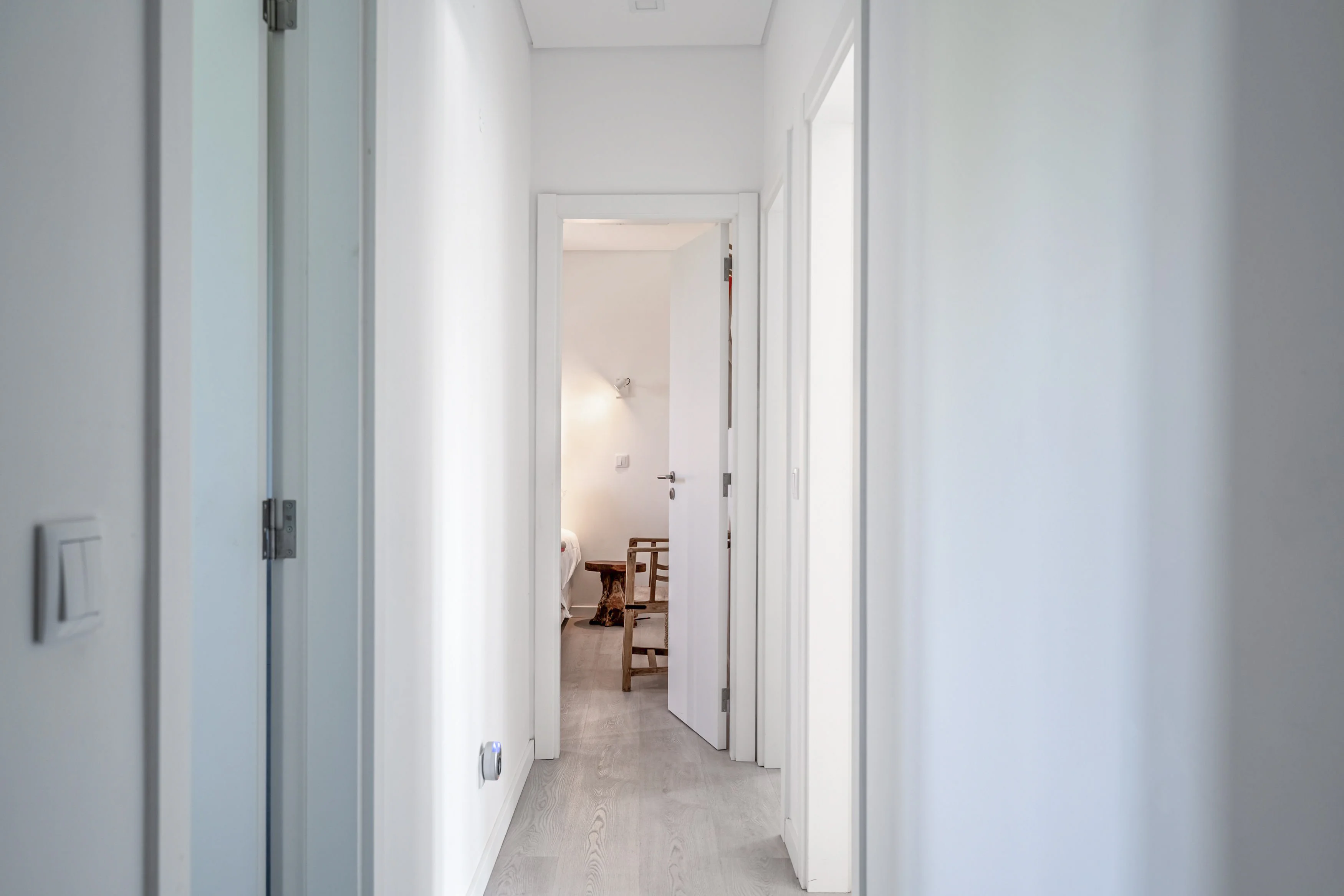 White hallway leading to bedroom with rustic bench and reading sconce
