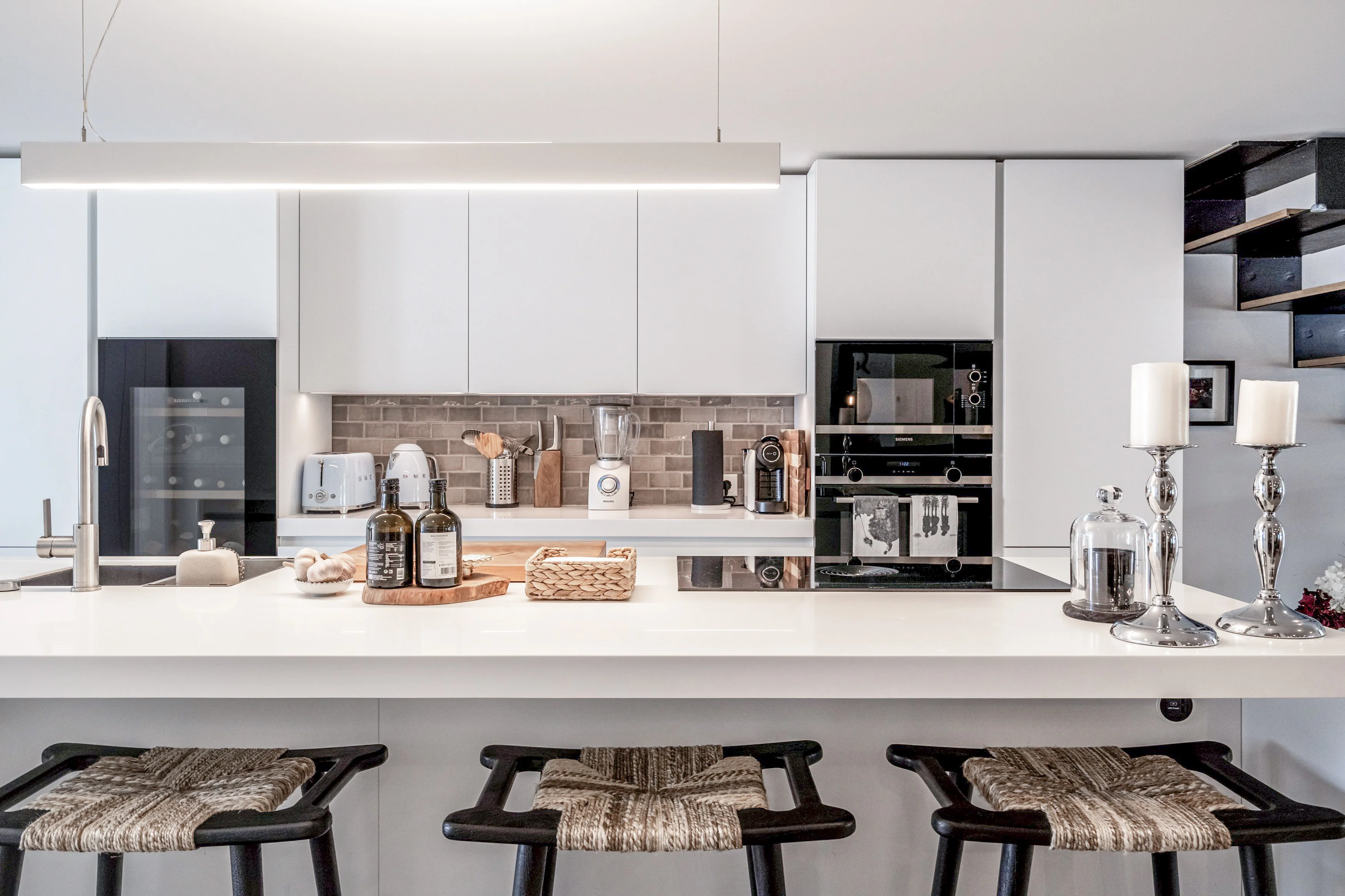 Modern white kitchen with waterfall island, woven bar stools and Smeg appliances