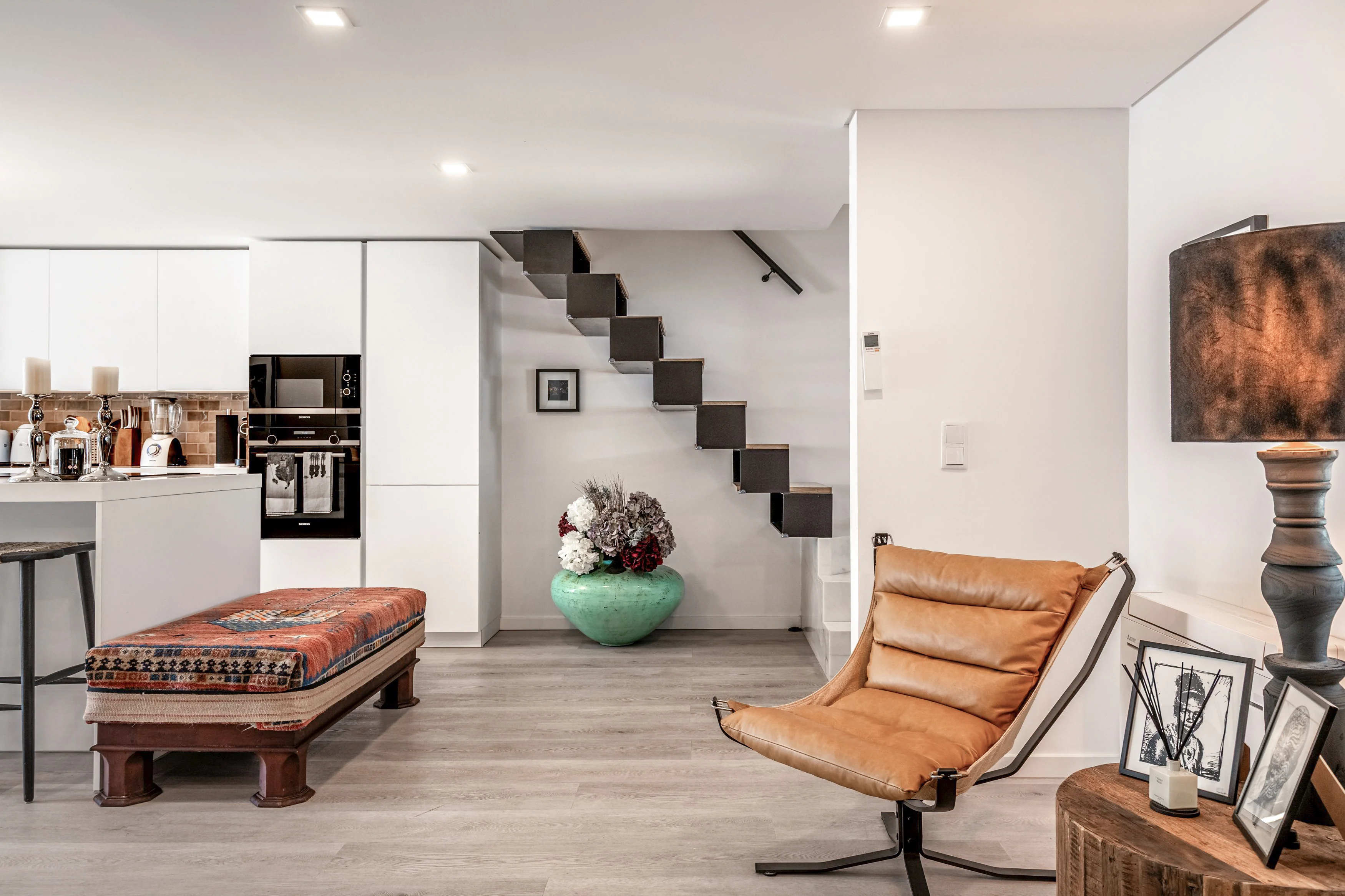 Open-plan kitchen and living area with white island, Barcelona chair and floating staircase