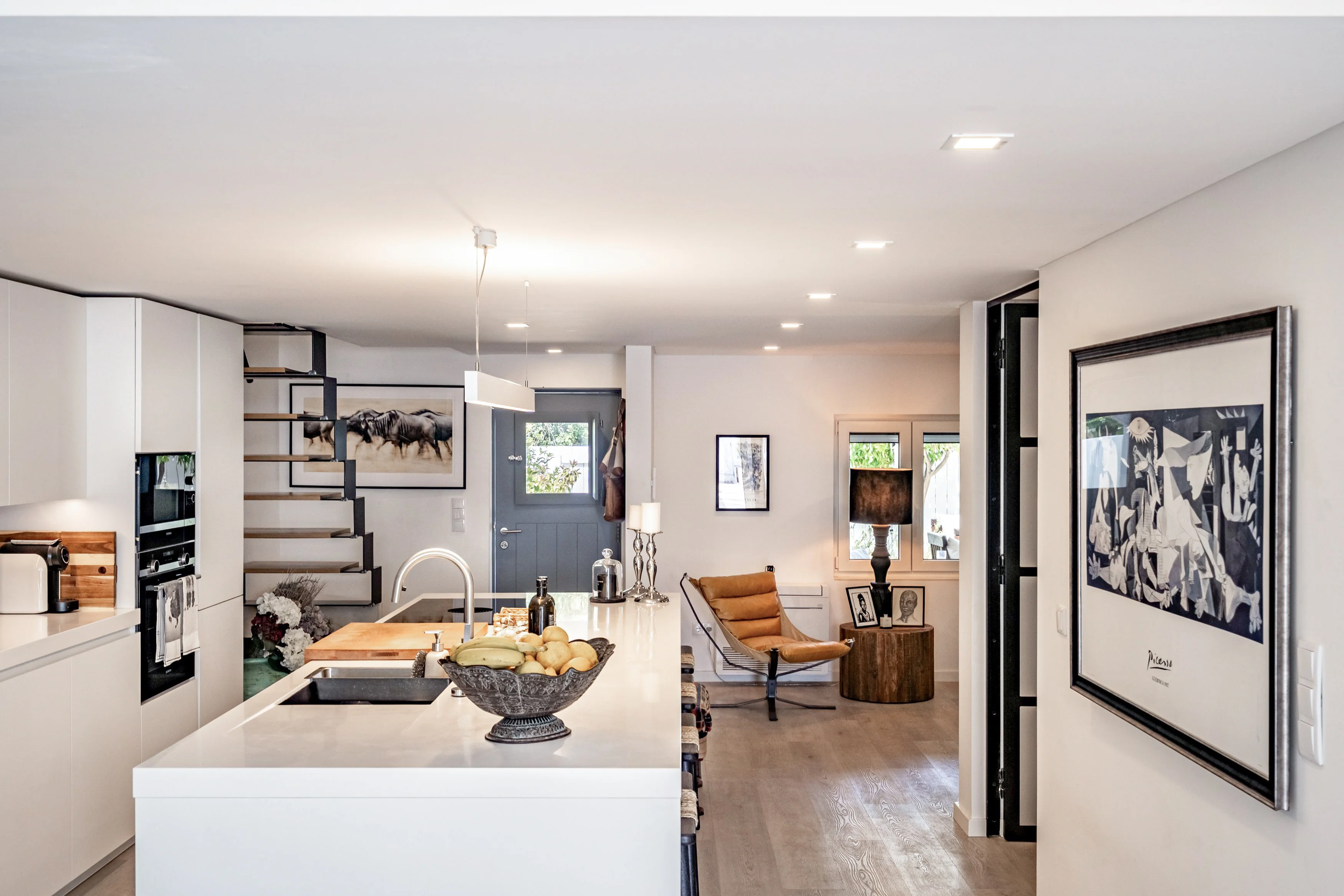 Open-plan kitchen and living room with floating staircase, white island and leather lounge chair
