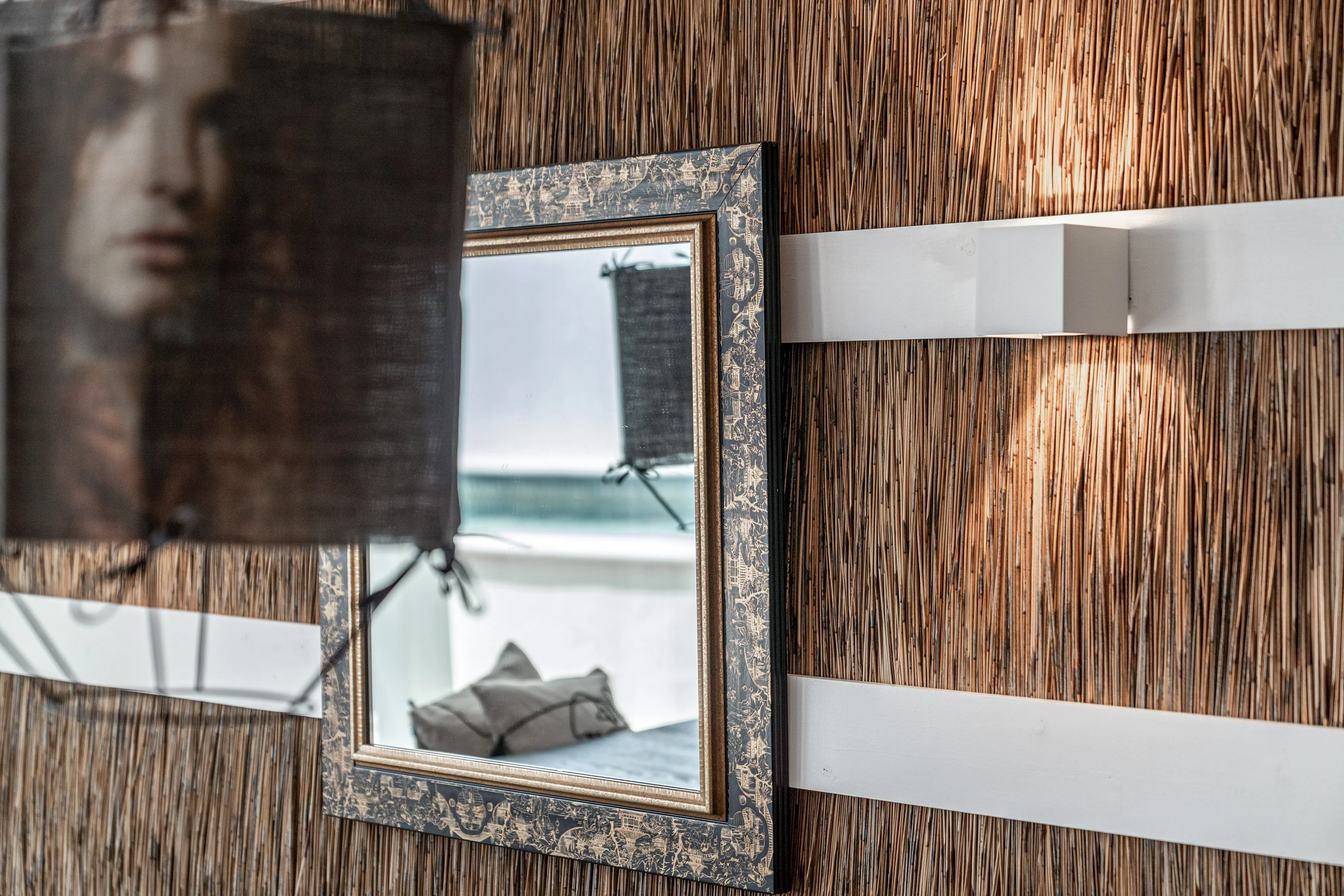 Detail: ornate black-and-gold mirror on reed/thatch wall with bathroom reflected