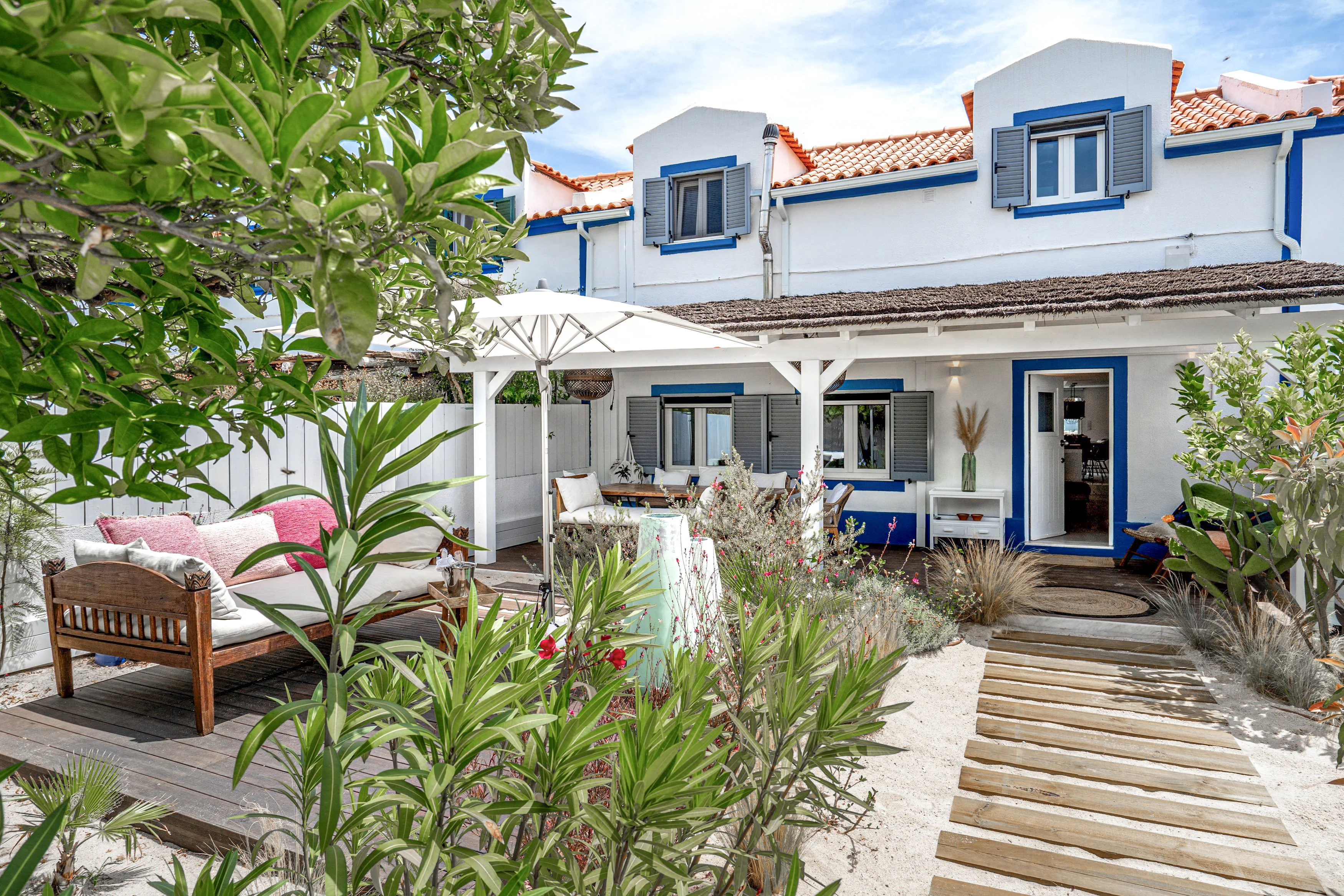 Courtyard terrace with thatched pergola, daybed, dining table and landscaped coastal garden